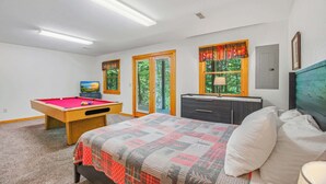 Un dormitorio con mesa de billar, cama, cómoda y ventana con vistas a árboles.