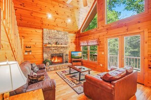 Ein Holzblockhaus-Interieur mit Kamin aus Stein, Ledermöbeln und einem Fernseher.