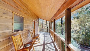 Una cabaña de madera con un porche, sillas de madera y una ventana.