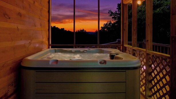 Una cabaña de madera con un jacuzzi y un ventanal grande con vistas a un atardecer.