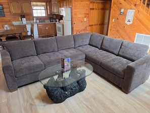 A modern living room with a sectional sofa, a glass coffee table, and wooden flooring.