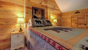 Ein Zimmer mit Holzwänden, einem Bett, zwei Nachttischlampen, einem Nachttisch, einem gerahmten Bild und einer Tür mit Wappen.