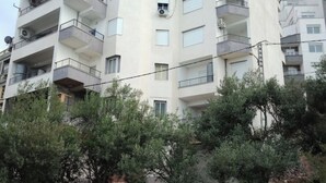 Un immeuble résidentiel à plusieurs étages, doté de balcons, de paraboles de télévision par satellite et offrant une vue sur les arbres environnants.