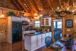 A spacious kitchen with wooden cabinets, a large island, and a dining area with chairs and a table. - Mtn Getaway, Sleeps 12・Spectacular Views・Hot Tub (Sevierville)
