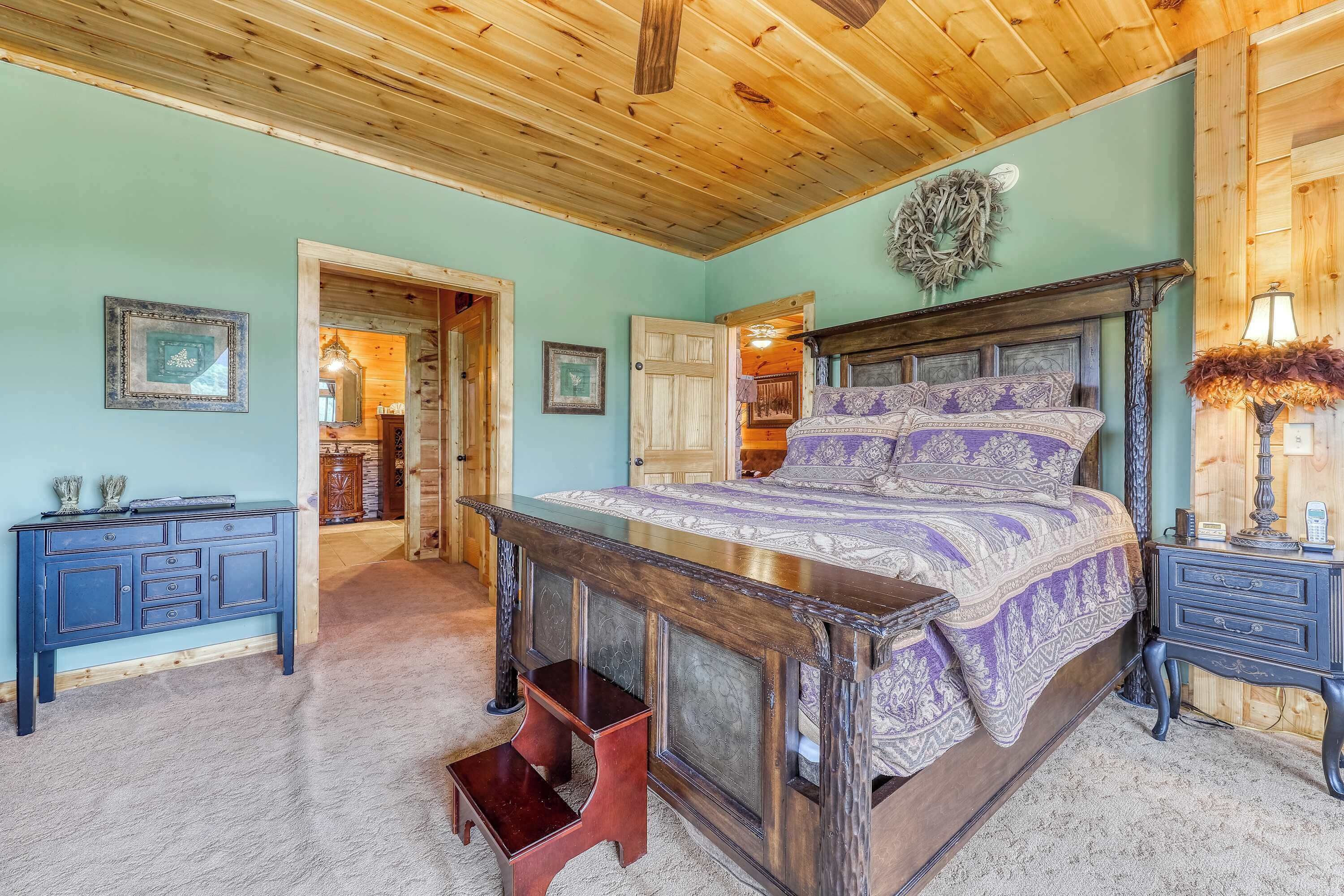 A bedroom with a wooden ceiling, a bed with patterned bedding, a nightstand, and a dresser.
