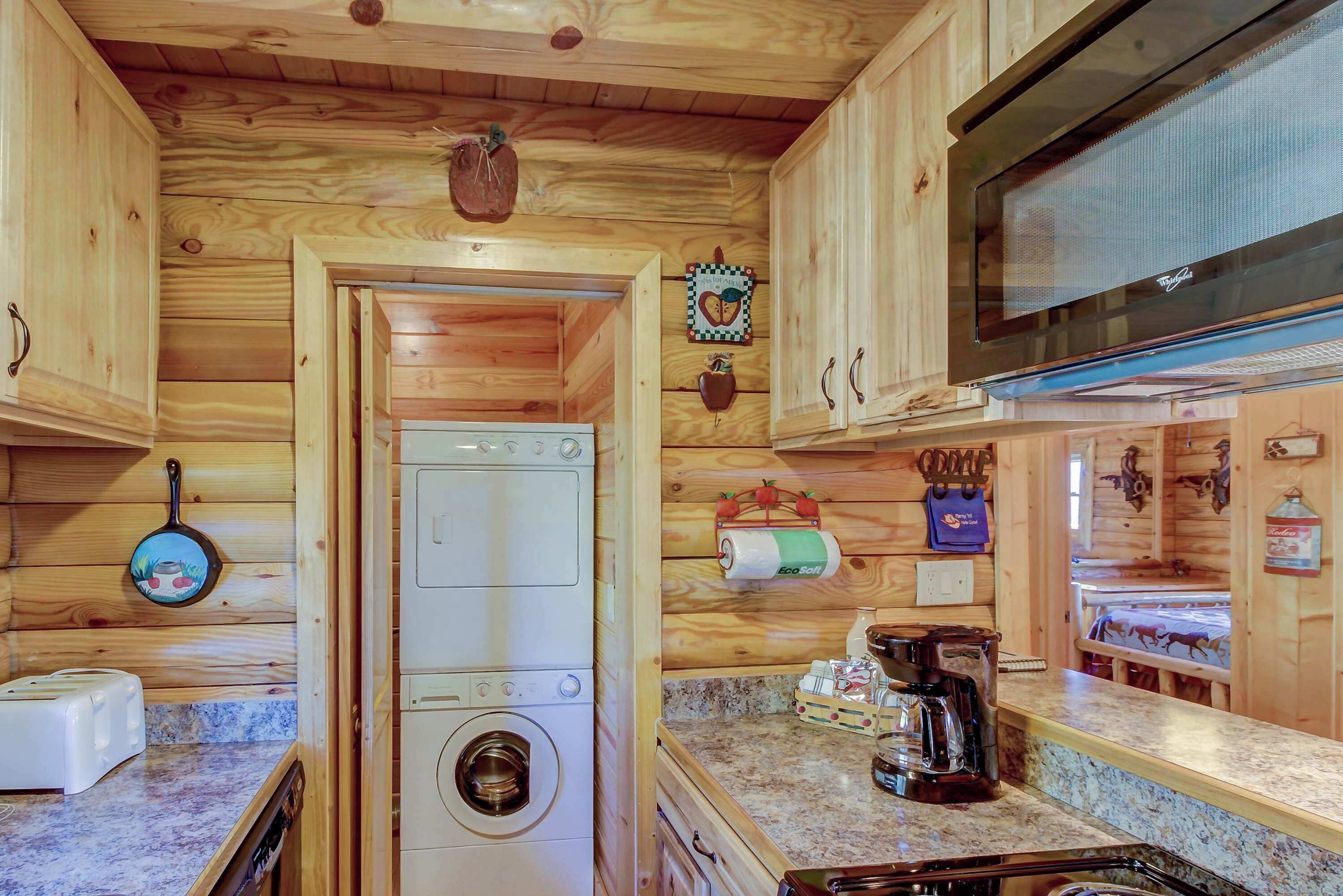 A compact kitchen with wooden cabinetry, a washing machine, a microwave, and a coffee maker.