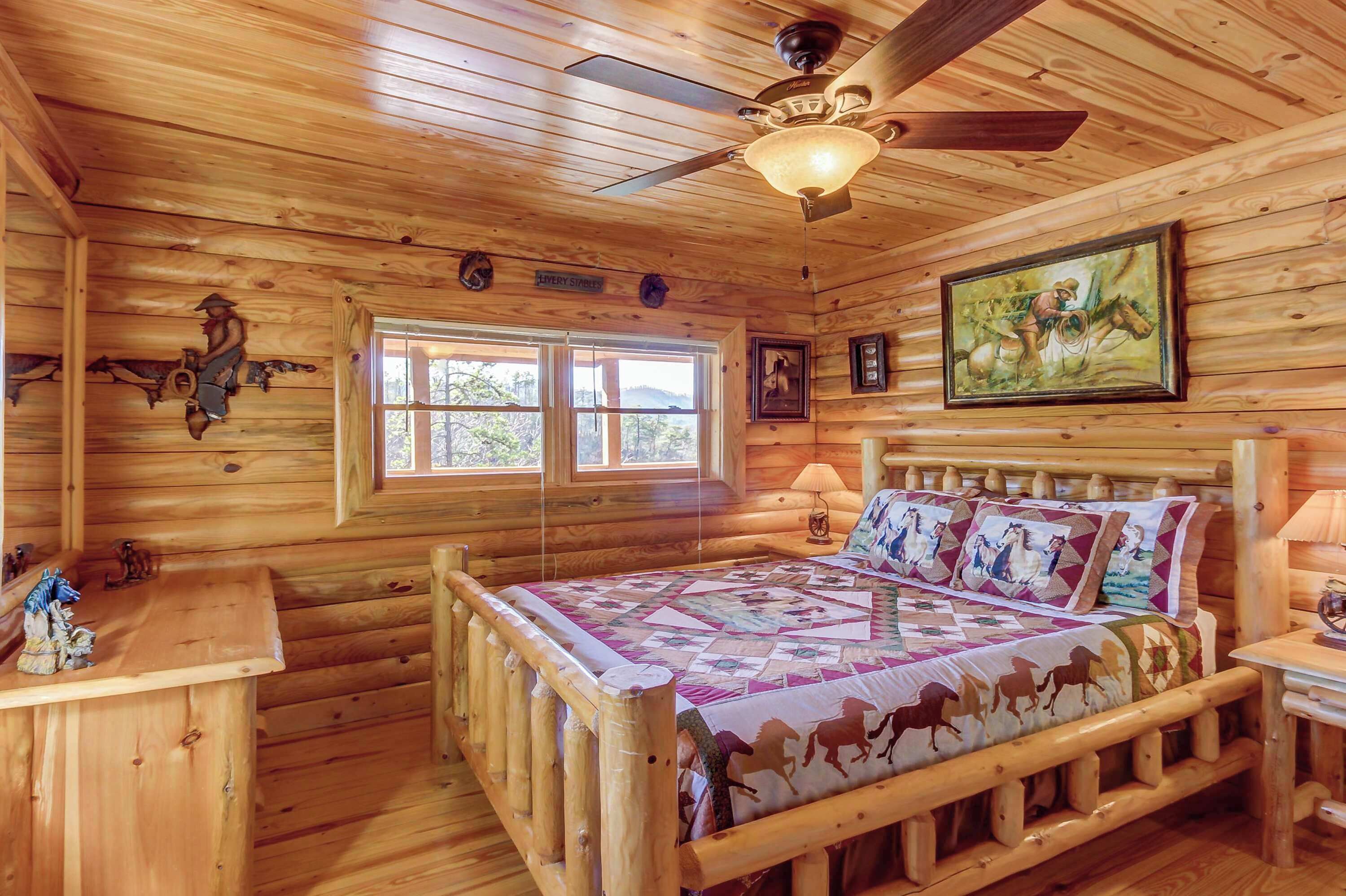A wooden cabin bedroom with a bed, a ceiling fan, a window, and a painting on the wall.