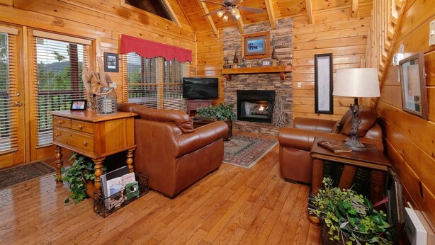 L’intérieur d’un chalet confortable, avec une cheminée, des canapés en cuir, un téléviseur et un mur en pierre.