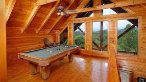 Un intérieur en bois avec une table de billard, de grandes fenêtres et un ventilateur de plafond.