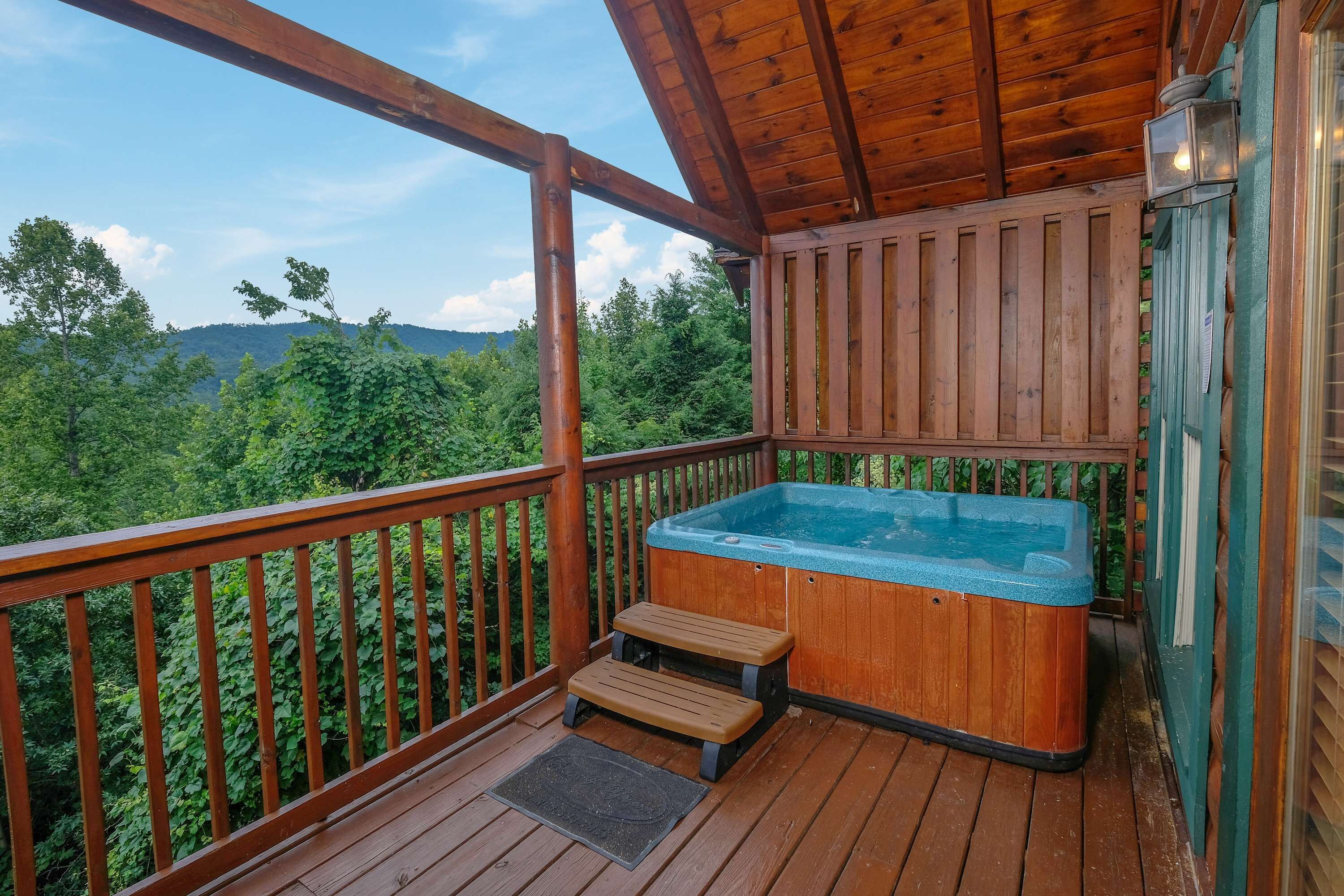 Een houten terras met een jacuzzi, houten traptreden en uitzicht op een bebost gebied.