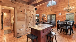 Un interior rústico de madera con una gran mesa de comedor de madera, taburetes de bar y una zona de cocina.