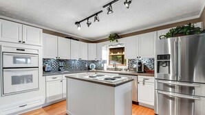 Une cuisine moderne avec des meubles blancs, un îlot central, des appareils en acier inoxydable et un pare-feu orné de carreaux bleus et blancs.