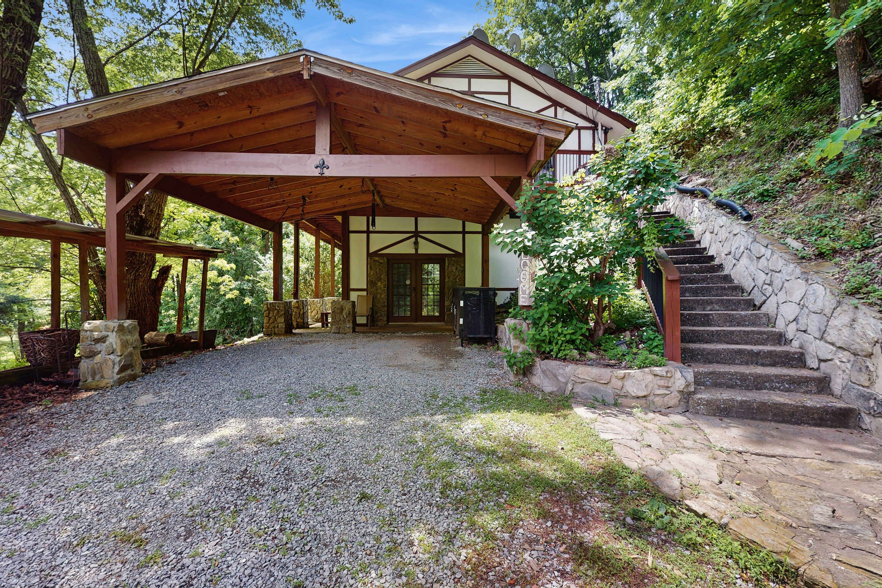 A rustic cabin with a covered porch, stone steps, and a gravel driveway.