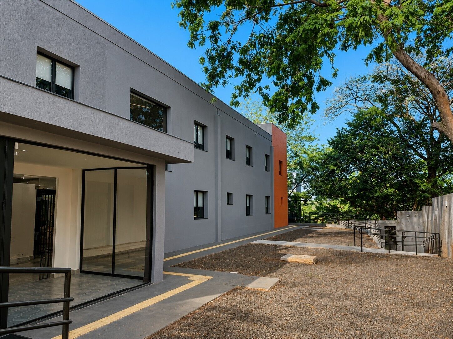 A modern building with a flat facade, large windows, and a gravel courtyard.