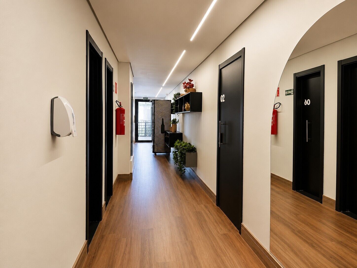 A hotel corridor with wooden flooring, black doors, and a fire extinguisher on the wall.