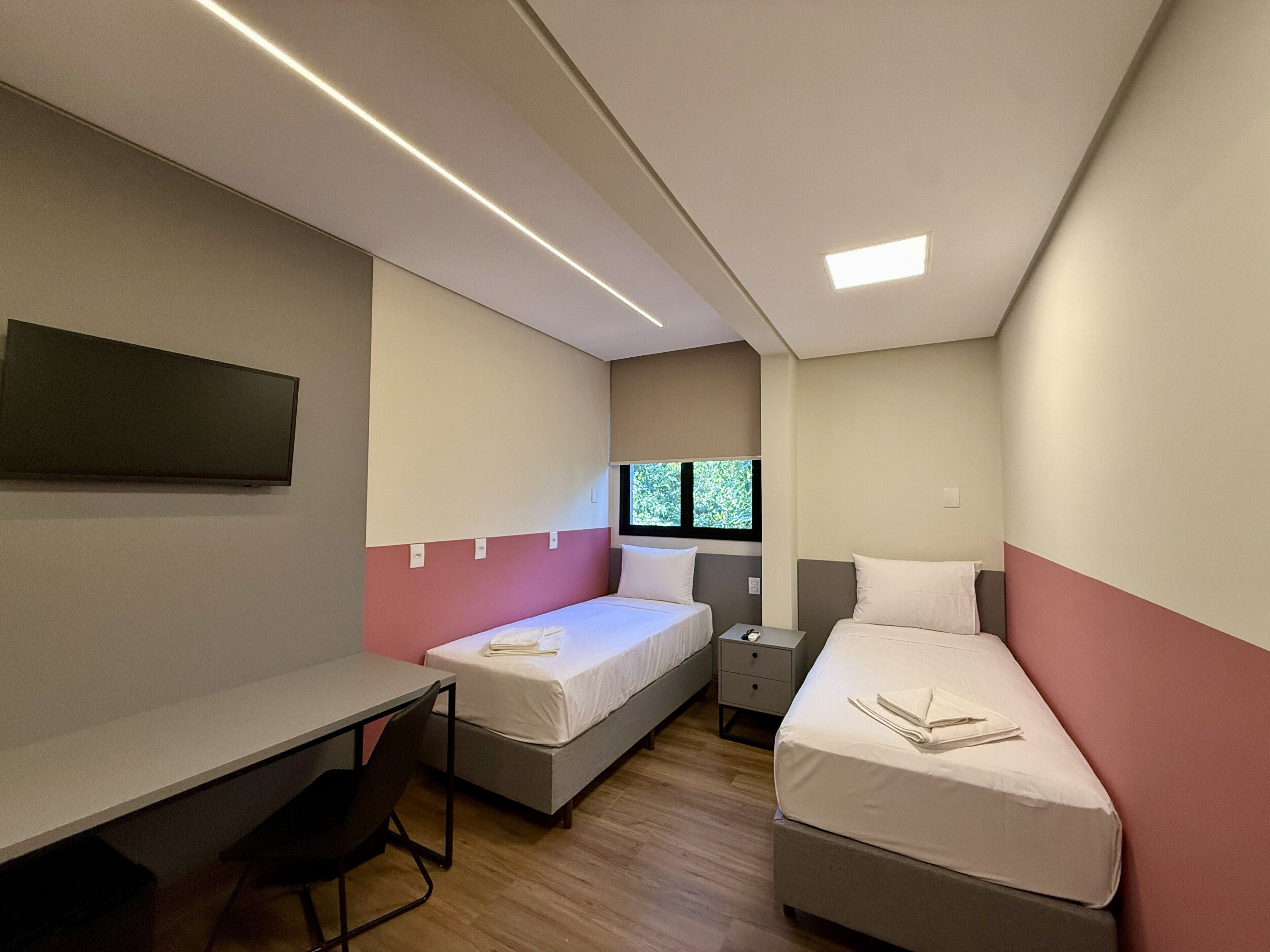A compact hotel room with two beds, a desk, a chair, and a TV.