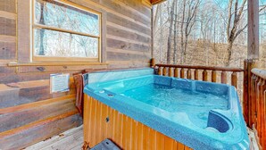 Eine Holzhütte mit Whirlpool und Fenster mit Blick auf einen Wald.