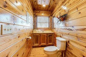 Une petite salle de bain en bois, aménagée dans une cabane, comprenant des toilettes, un lavabo et un meuble de rangement.