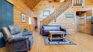 Ein Blockhaus-Interieur mit Holzvertäfelung, einem Ledersessel, einem blauen Sofa, einem Holztisch und einer Treppe.