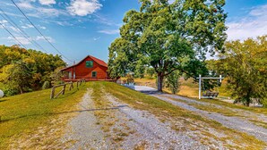 Ein rotes Bauernhaus mit grüner Tür, umgeben von Bäumen und einem Schotterweg.