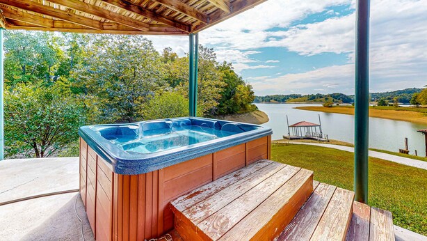 Ein Whirlpool unter einer hölzernen Pergola mit Blick auf einen See und Bäume.