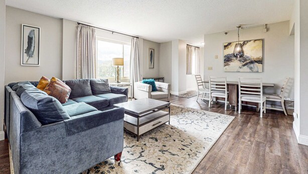 A modern living room with a grey sofa, a coffee table, and a dining area with white chairs and a table. - 2 All-Suite Condos, Sleeps & River View Balconies (Pigeon Forge)