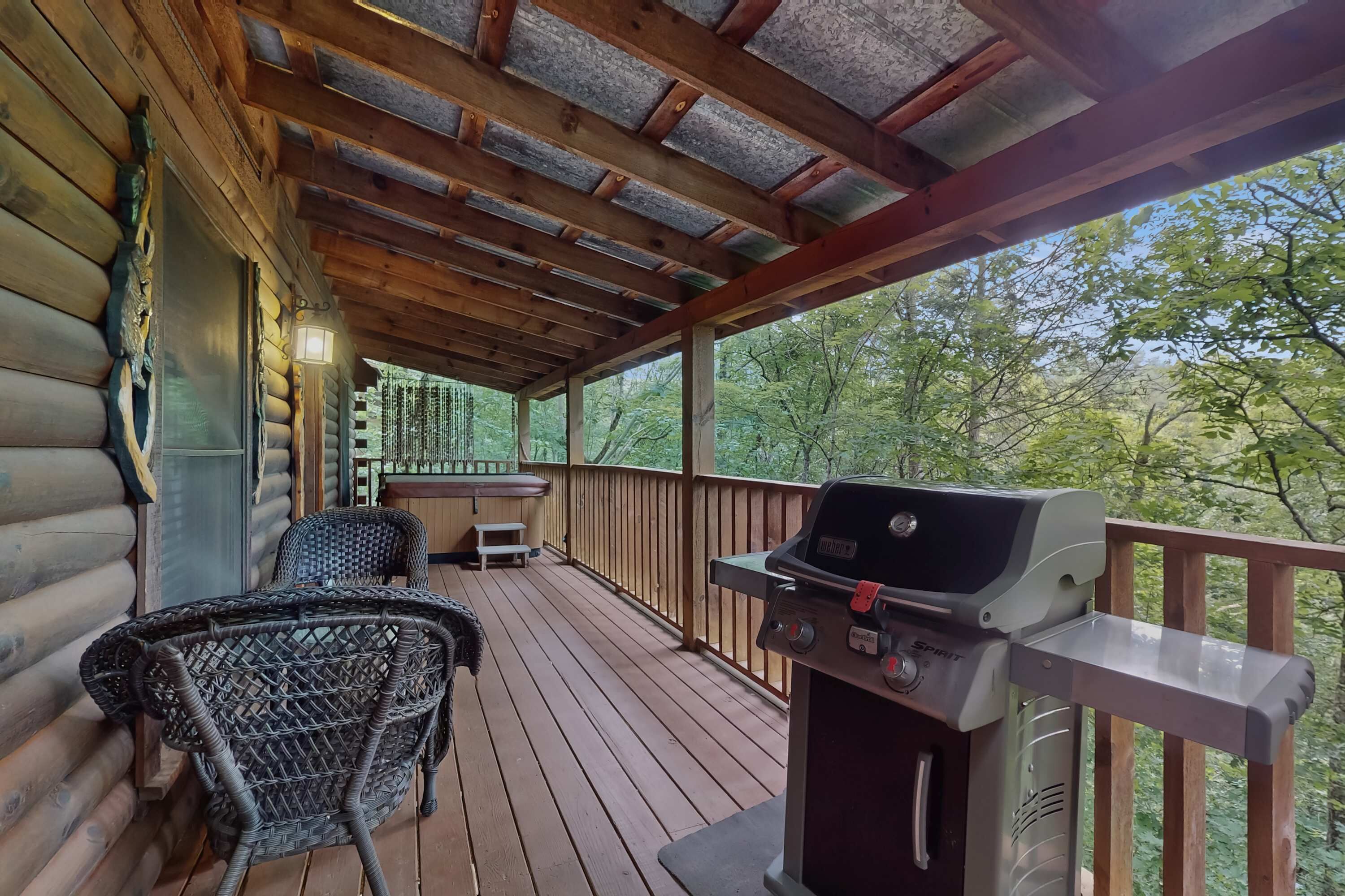 Eine überdachte Holzterrasse mit Grill, Korbmöbeln und Blick ins Waldgebiet.