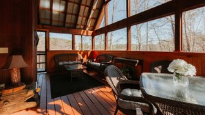Eine Holzterrasse mit Korbmöbeln, einem Glastisch und einer Blumenvase sowie einem Deckenventilator.