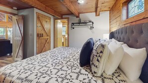 Ein Schlafzimmer mit einem großen Bett, Holzbalken an der Decke, einem Deckenventilator und einem Fenster mit Glasmalerei.