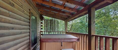Une cabane en bois avec un jacuzzi, une terrasse en bois et une vue sur la forêt.