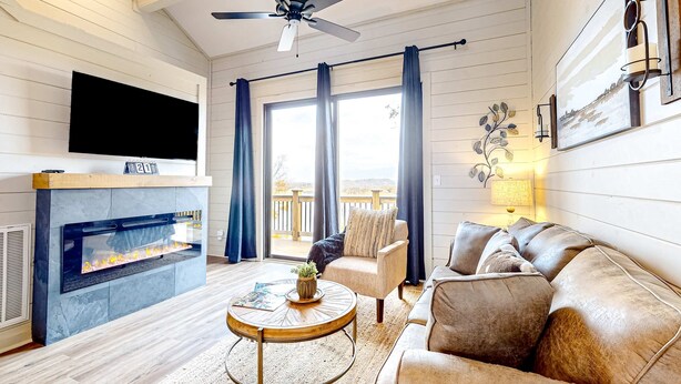 A living room with a fireplace, a ceiling fan, a sofa, and a television mounted on the wall. - Brand New Cabin Overlooking Douglas Lake・Hot Tub (Sevierville)