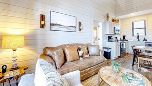A cozy living room with a brown leather sofa, a coffee table, and a dining area with a wooden table and chairs. A kitchen with white cabinets and a sink is visible in the background. - Brand New Cabin Overlooking Douglas Lake・Hot Tub (Sevierville)