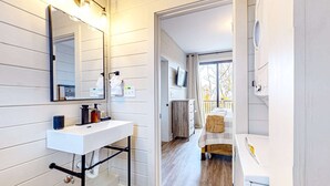 A modern bathroom with a white sink, mirror, and vanity, a washing machine, and a view of a balcony with a wooden deck. - Brand New Cabin Overlooking Douglas Lake・Hot Tub (Sevierville)