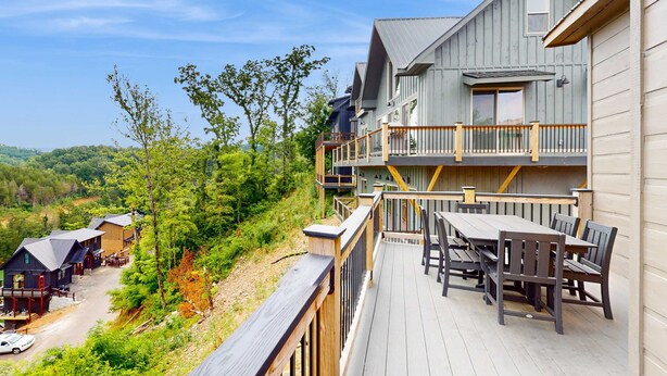 Een houten terras met buitenmeubilair, een balkon met een hekwerk en uitzicht op een bebost gebied.