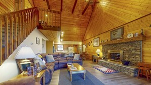 L’intérieur d’un chalet confortable en bois, avec un salon, une cheminée en pierre et un escalier.