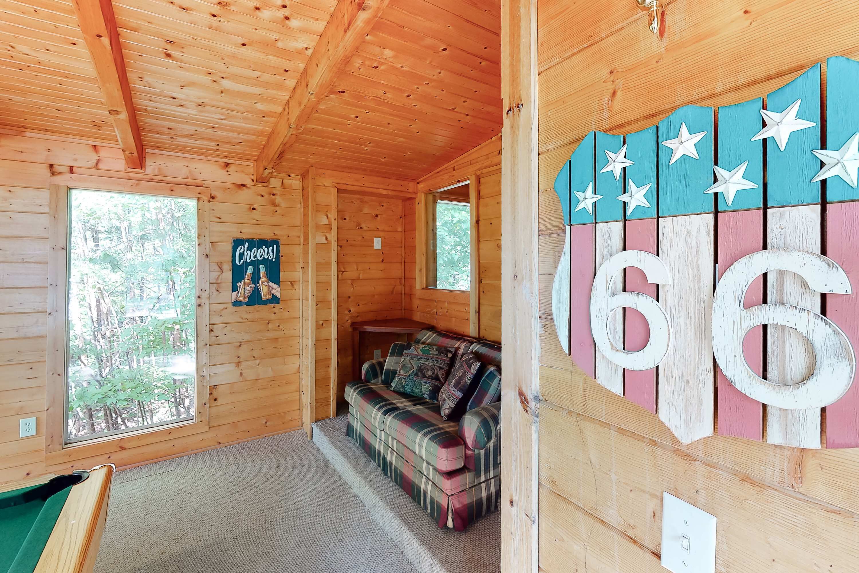 A cozy cabin interior with a plaid sofa, a pool table, and a 'Cheers!' sign.