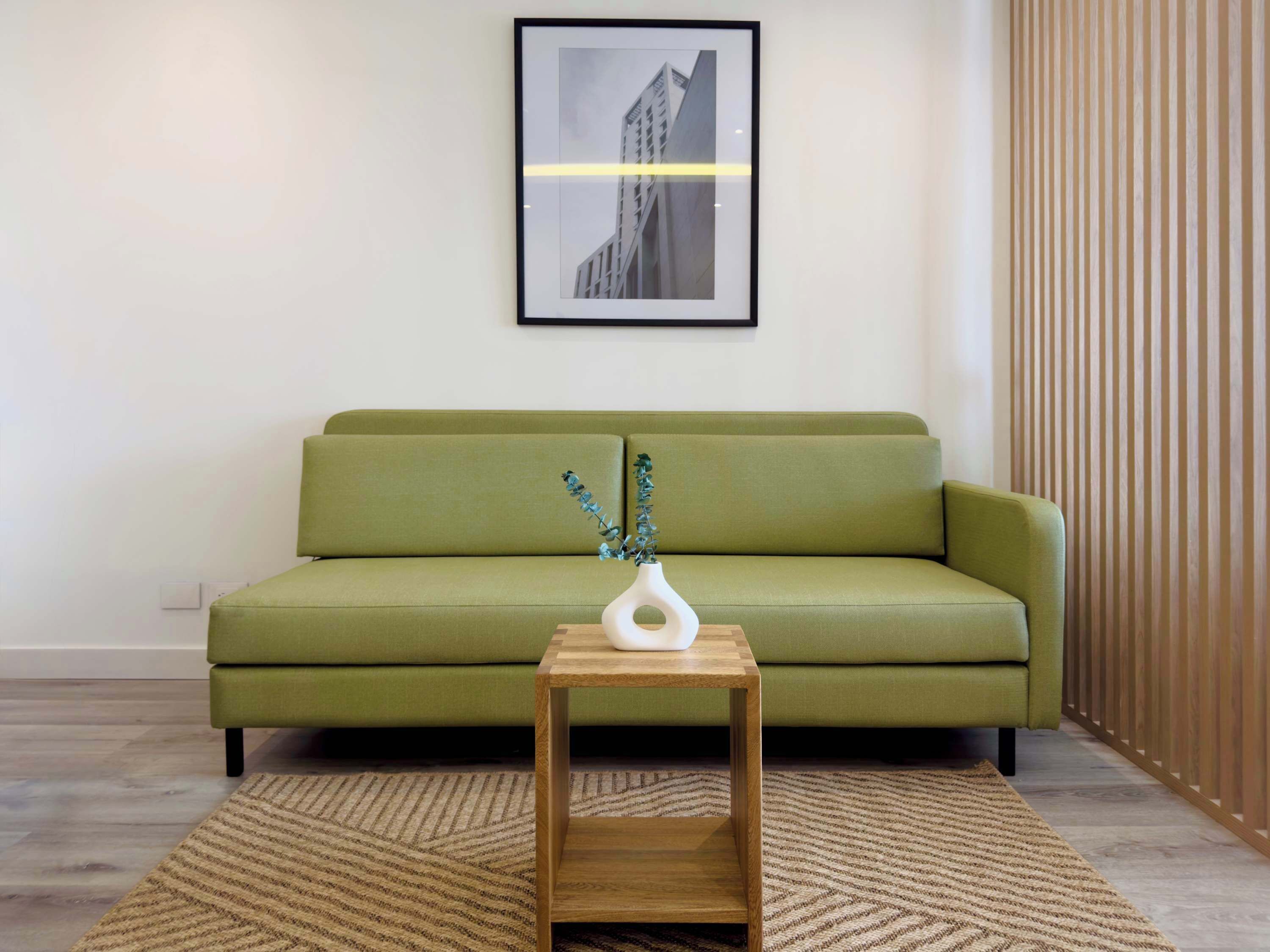 Ein grünes Sofa, ein Holznachttisch und ein gerahmtes Bild an der Wand.