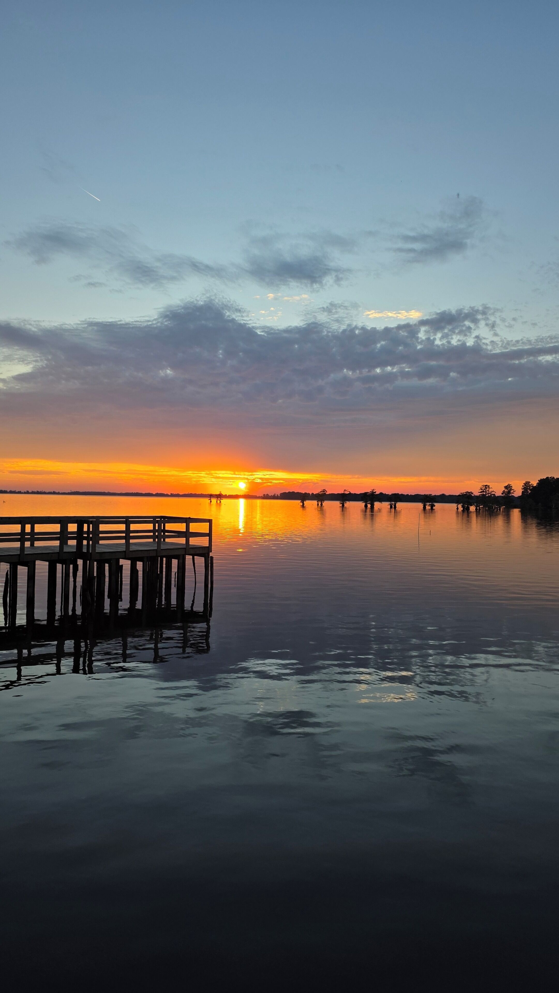 Une jetée en bois s’étendant sur une étendue d’eau calme, avec un coucher de soleil en arrière-plan.