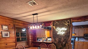 Ein rustikaler Essbereich mit Holztisch und -stühlen, eine Küche im Hintergrund und ein Neonzeichen an der Wand.