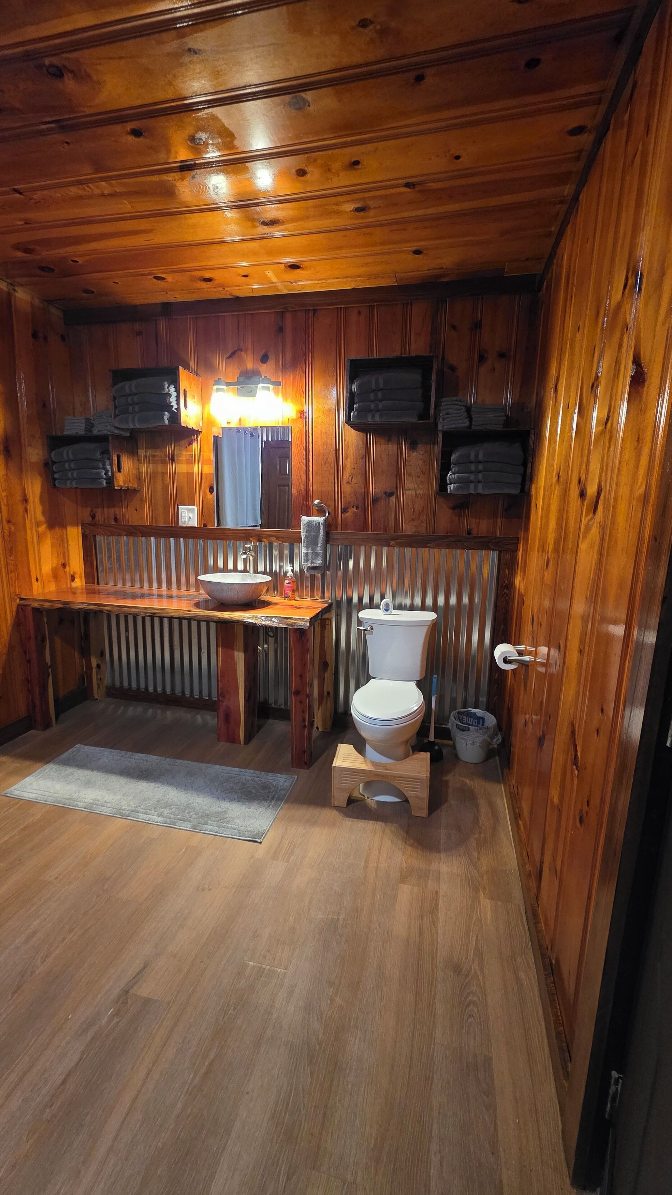 Een houten badkamer met een houten bankje, een wastafel, een toilet en een spiegel.