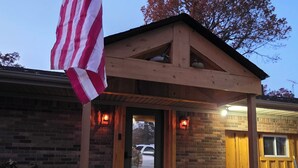 Eine Holzhütte mit Veranda, einer amerikanischen Flagge und einer Ziegelaußenwand.