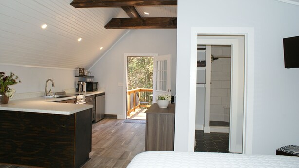 A modern kitchen with a central island, a dining area with a wooden table, and a bedroom with a large bed. - Norah's Nest 
"Step into your own private retreat!" (WOODSTOCK)