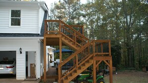 A two-story wooden deck with a staircase leading to a garage. - Norah's Nest 
"Step into your own private retreat!" (WOODSTOCK)
