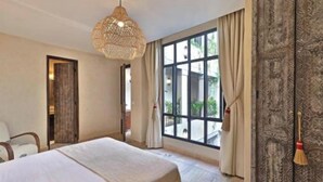 A hotel room with a large bed, a hanging light fixture, a window with curtains, and a patterned wall. - Riad dar Tayri (Marrakech)
