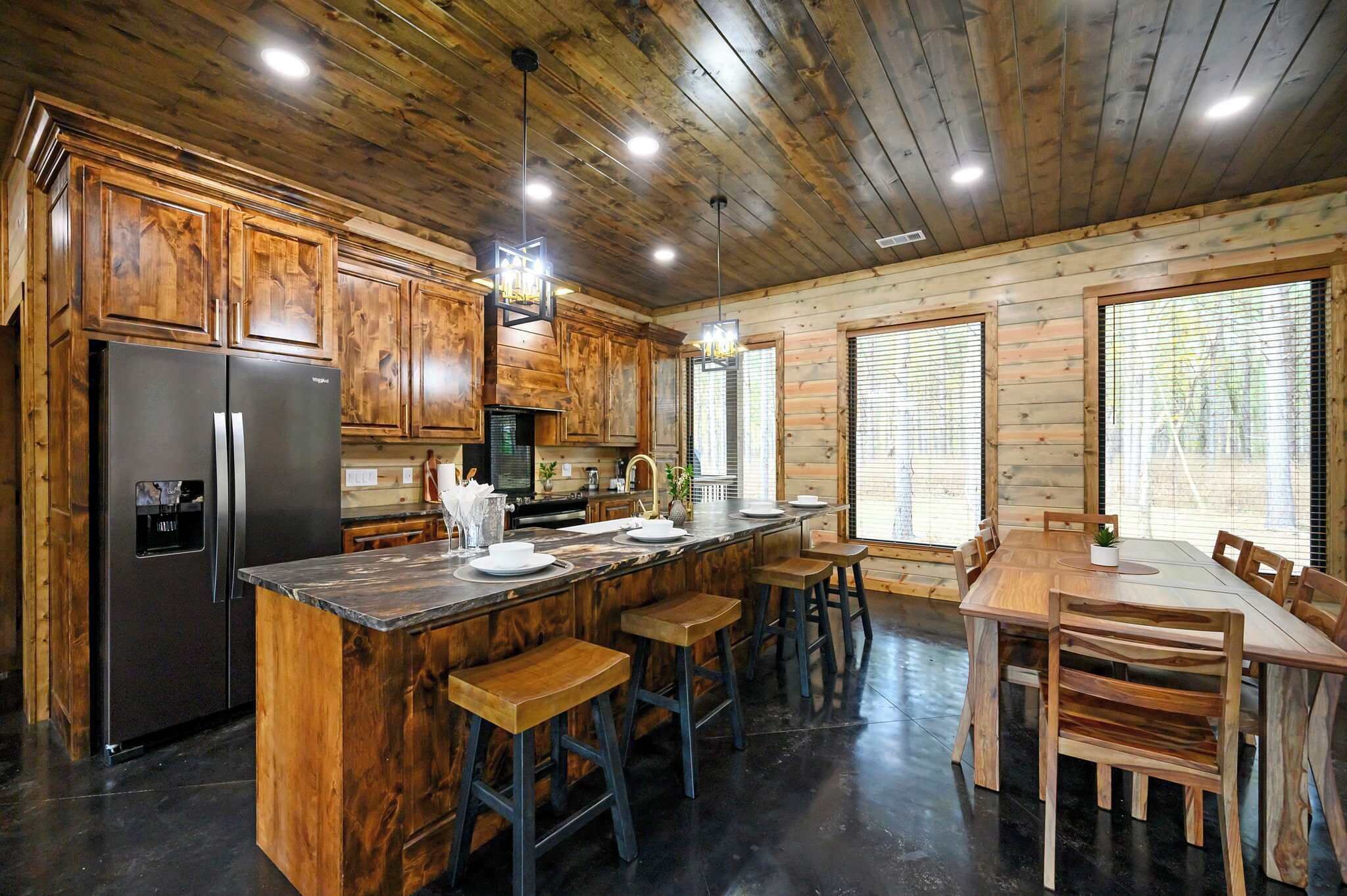 A kitchen with wooden cabinets, a refrigerator, a sink, and a dining area with a table and chairs.