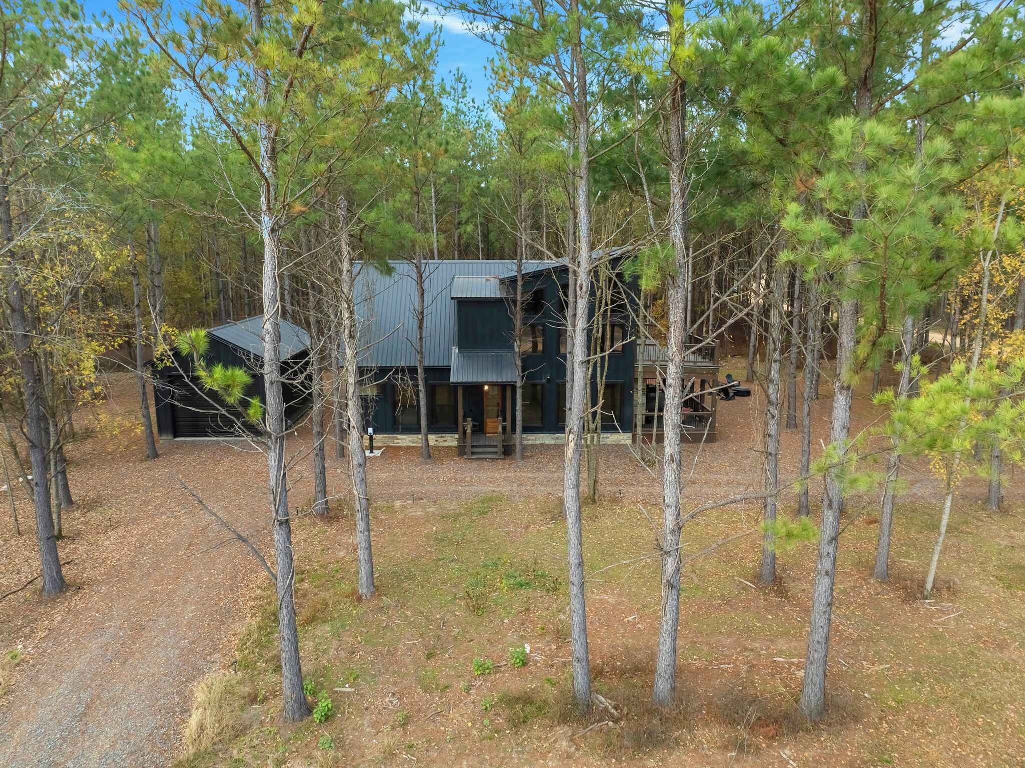 A modern two-story house surrounded by tall pine trees.