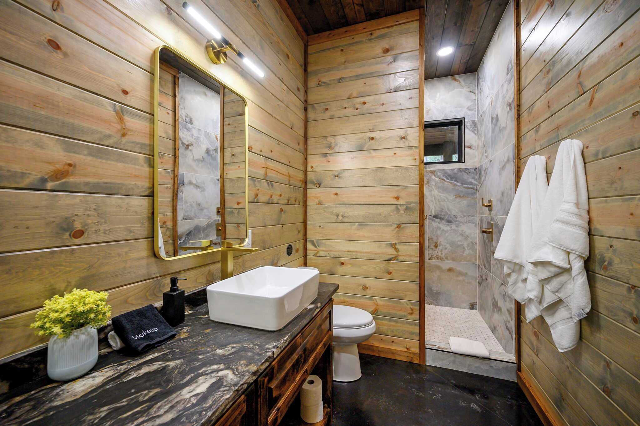 Un baño con paredes de madera, un lavabo de mármol, un inodoro y una zona de ducha.