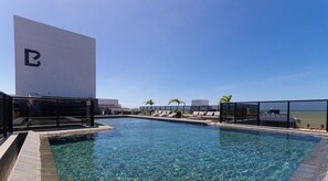 A rooftop pool with clear blue water, lounge chairs, and a view of the beach. - Way Tambaú Suites (João Pessoa)