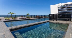 A rooftop pool with clear water, lounge chairs, and palm trees. - Way Tambaú Suites (João Pessoa)