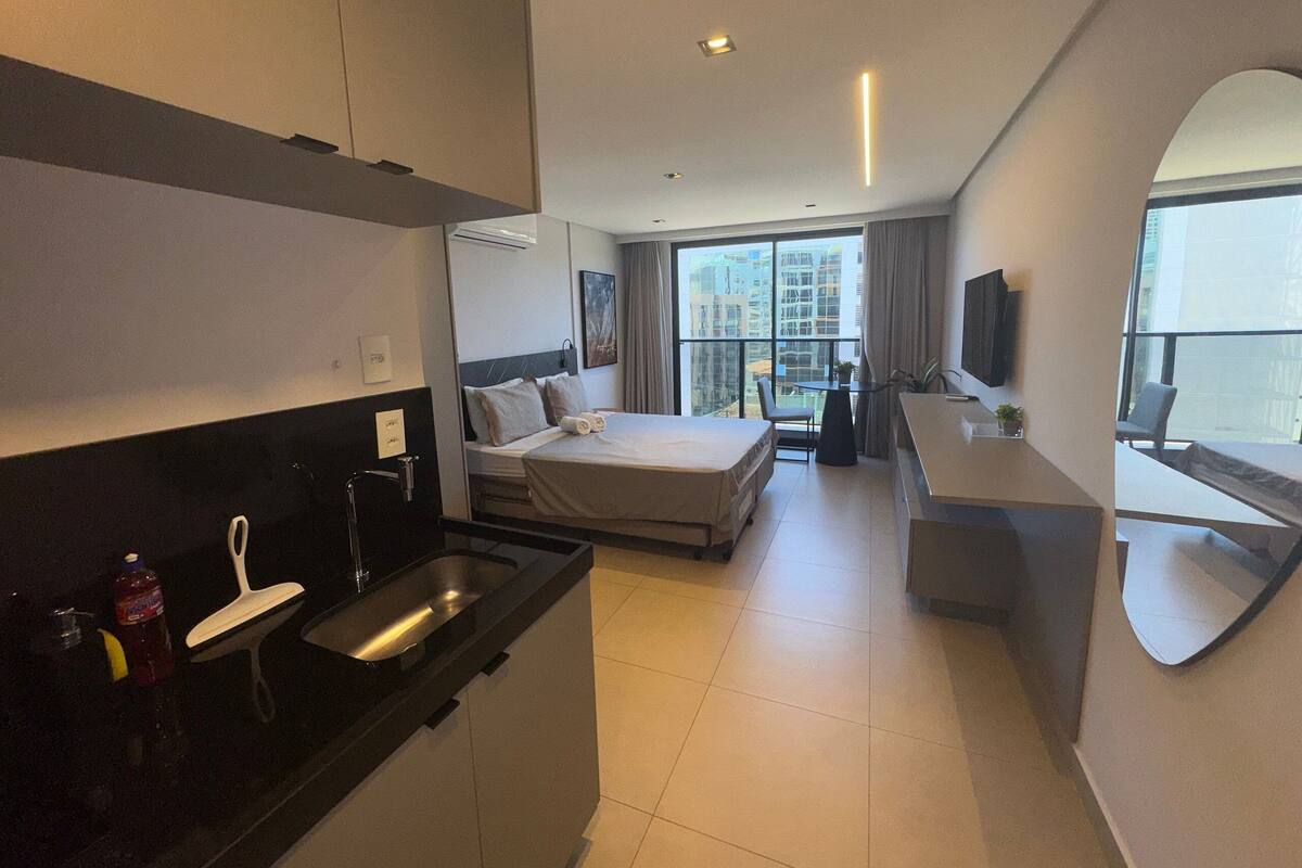 Une chambre d’hôtel équipée d’un lit, d’un bureau, d’une chaise, d’une petite table, d’un lavabo et d’une grande fenêtre donnant sur des immeubles.